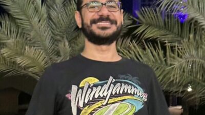 Hombre sonriente con camiseta de Windjammers frente a palmeras